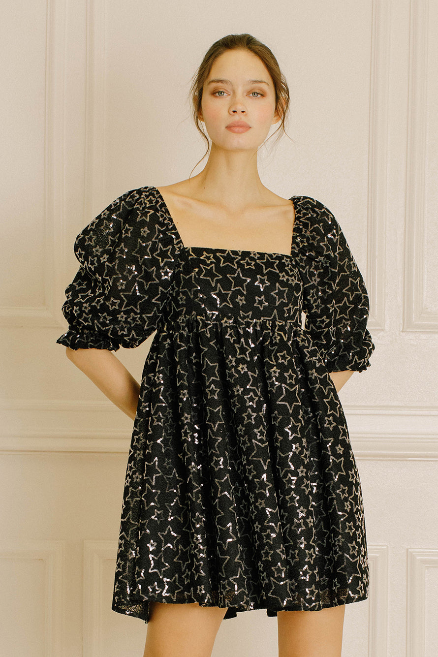 Woman wearing a black dress with star pattern against a neutral wall