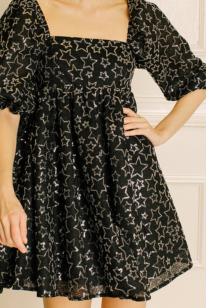 Black dress with star pattern worn by a person against a neutral background