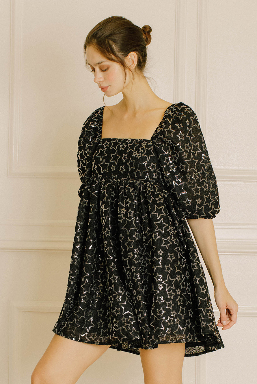 Woman wearing a black dress with sequin star pattern against a neutral background