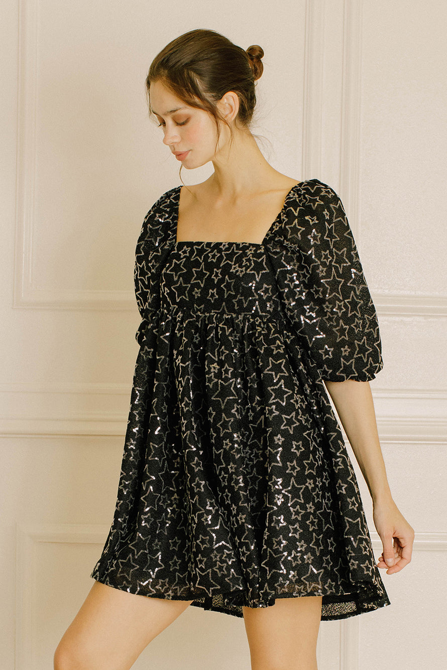 Woman wearing a black dress with sequin star pattern against a neutral background