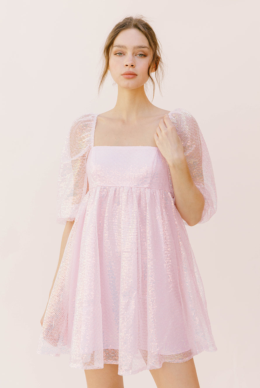 Woman wearing a pink sequin dress with sheer sleeves against a neutral pink background