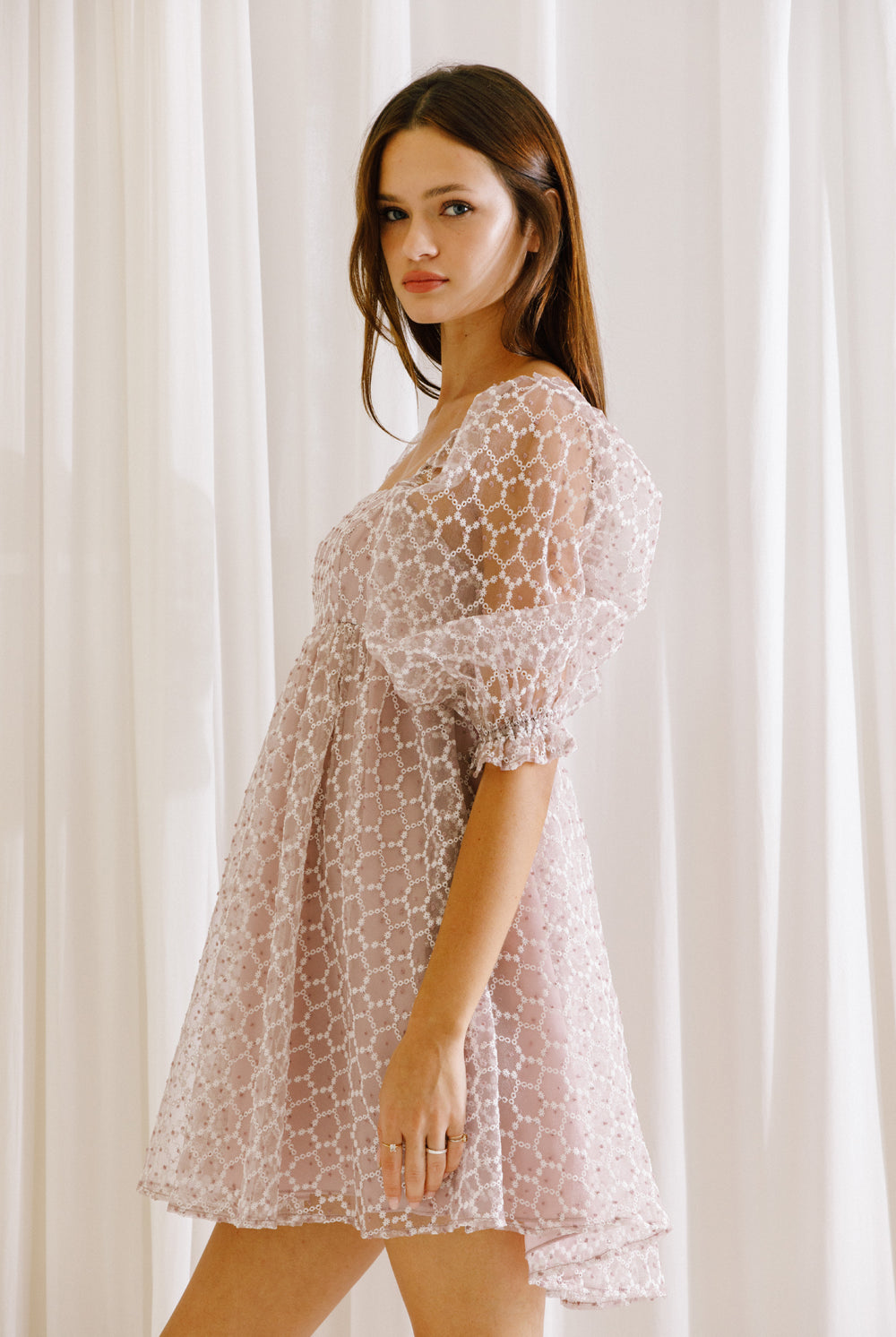 Side view of a model wearing a lilac mini dress with mini daisies embroidery and puffy sleeves
