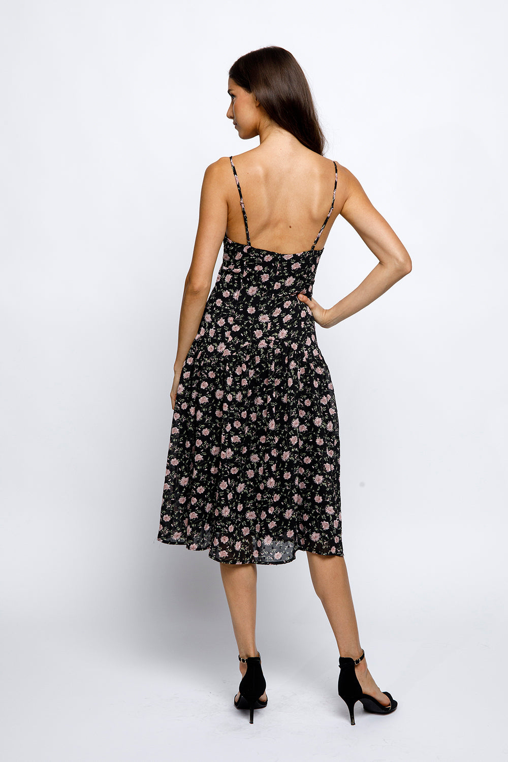 Back view of a woman wearing a black floral dress on a white background