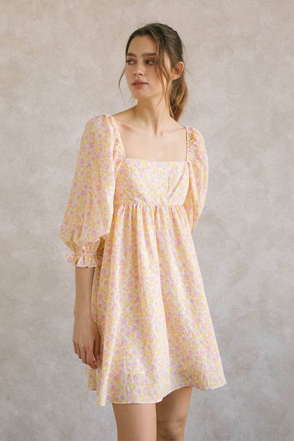 Woman wearing a pink and orange floral dress against a plain background
