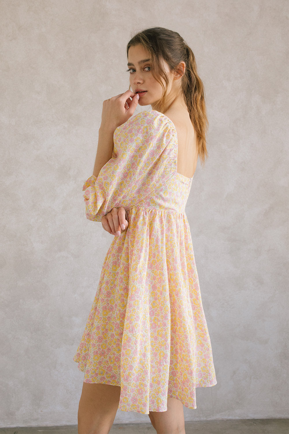 Side view of a woman wearing a pink and orange floral dress against a plain background