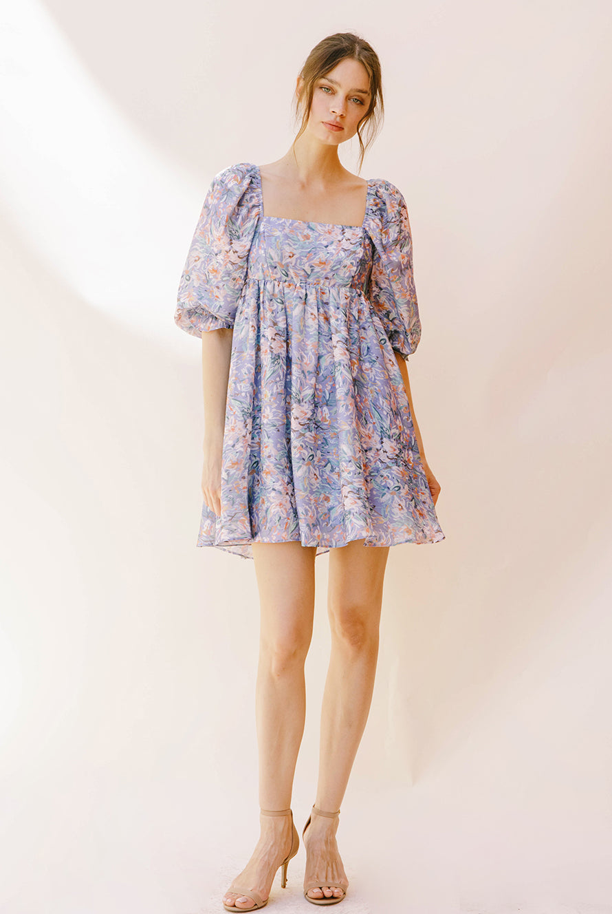 Woman wearing a purple paint stroke print dress with beige high-heels against a plain background