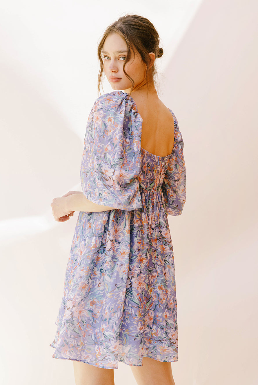 Back view of a woman wearing a purple paint stroke print dress against a plain background