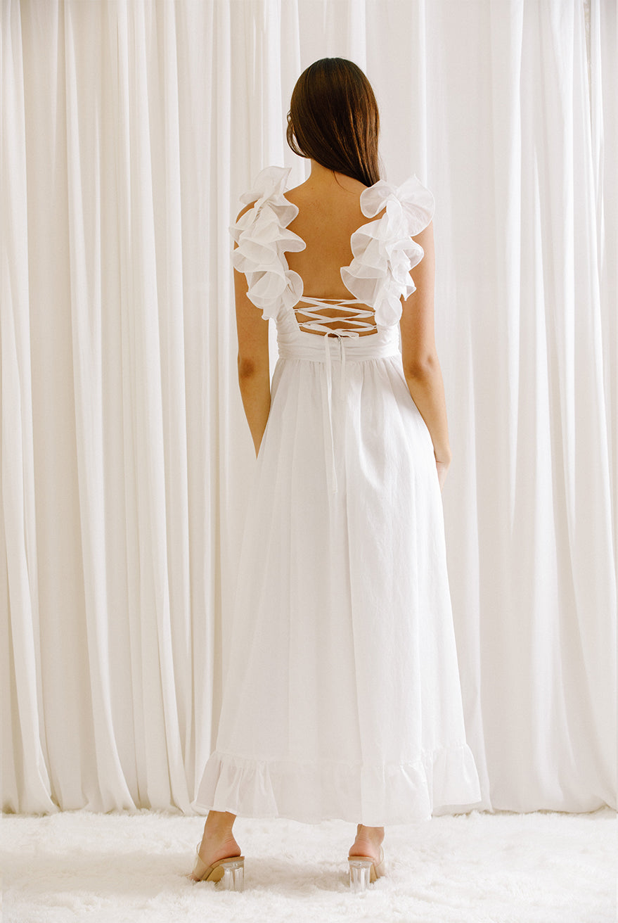 Back view of a woman wearing a white dress standing in front of white curtains