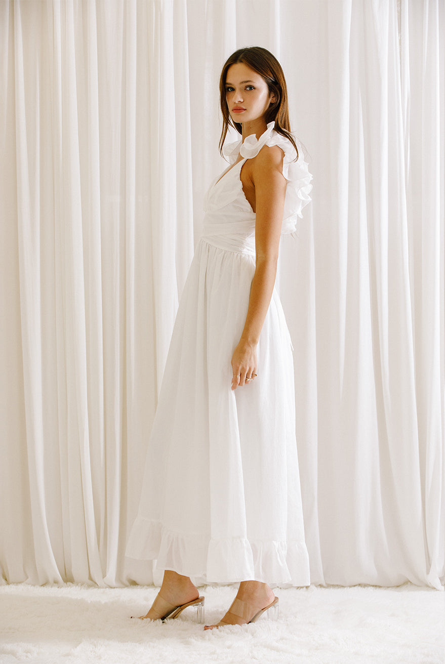 Side view of a woman wearing a white dress standing in front of white curtains
