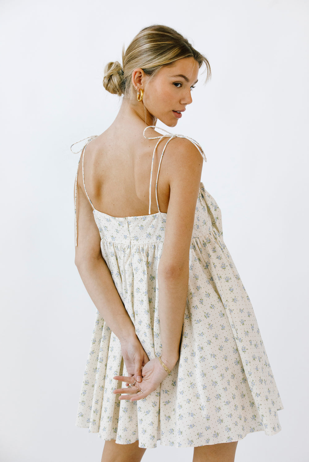 Back view of a woman wearing a floral dress with thin straps on a white background