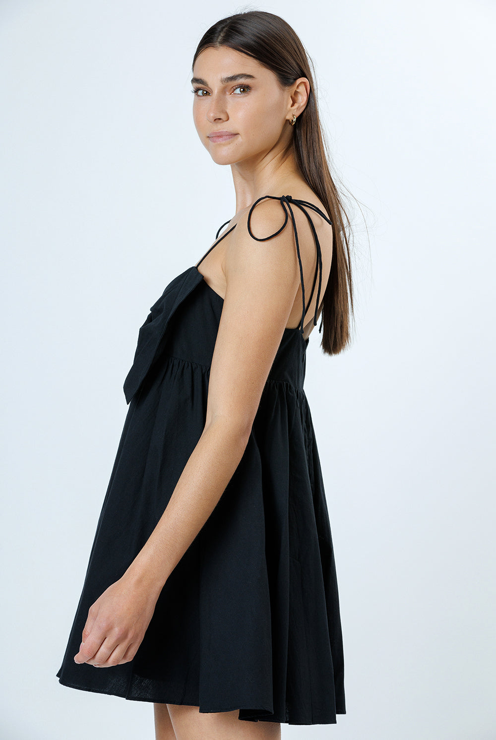 Side view of a woman wearing a black dress with thin straps on a white background