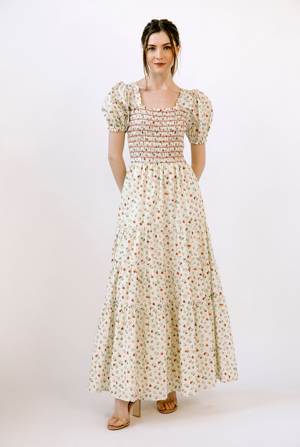 Woman wearing a floral maxi dress and beige heels on a white background
