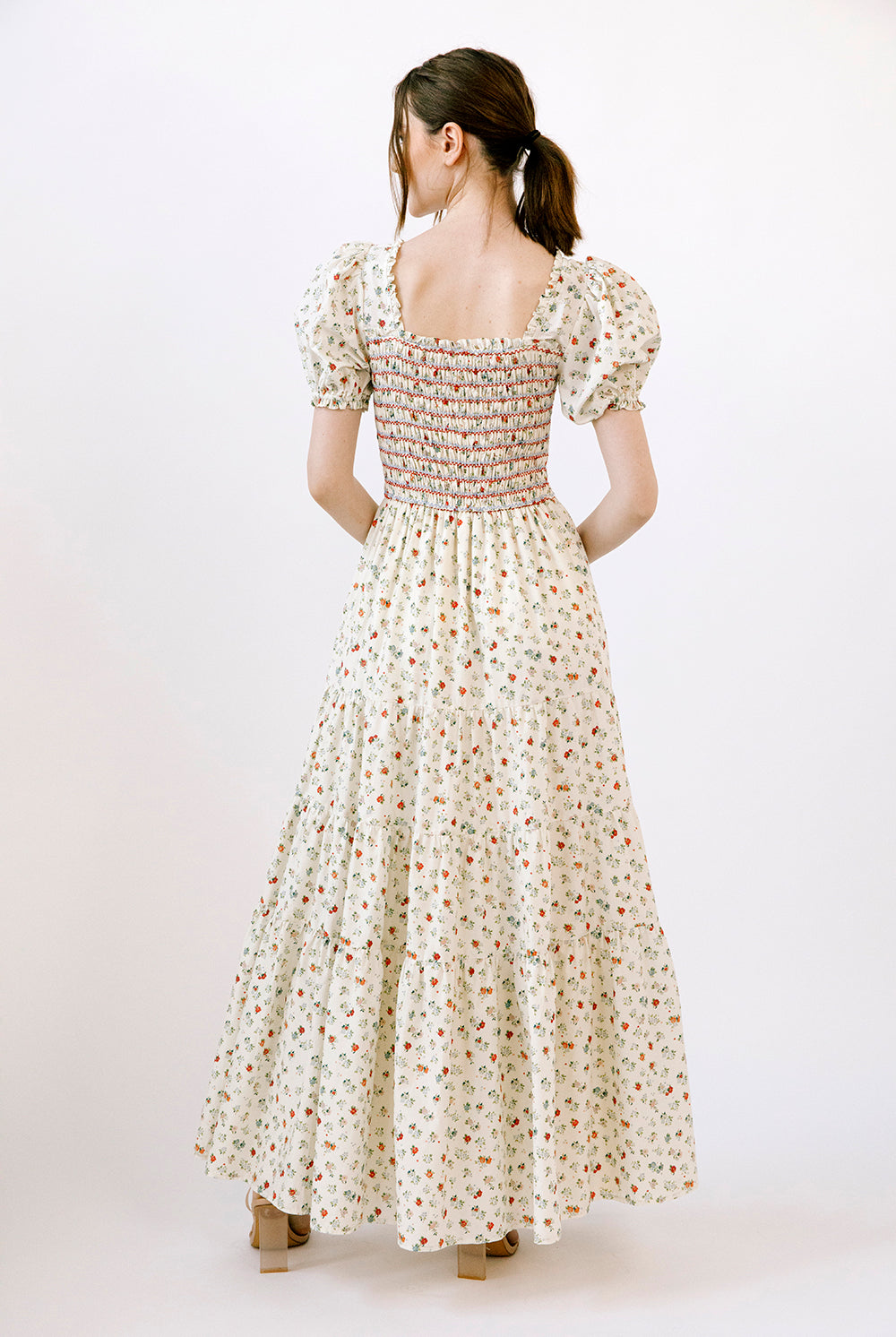 Back view of a woman wearing a cream and red floral dress on a white background