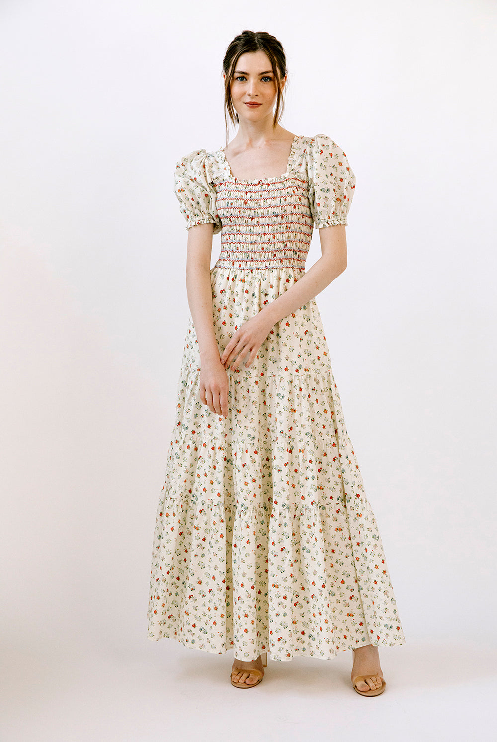 Woman wearing a cream and red floral maxi dress on a white background