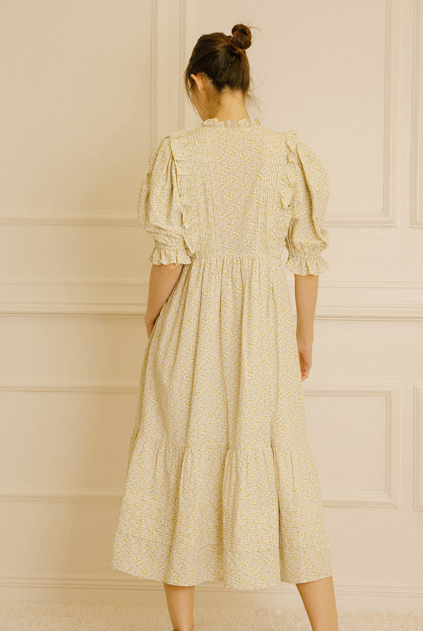 Back view of a woman wearing a light-colored dress with floral pattern against a neutral wall.