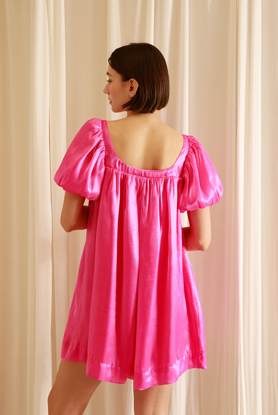 Back view of a woman wearing a pink nightgown silhouette dress against a beige wall