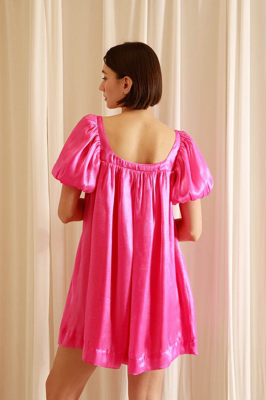 Back view of a woman wearing a pink nightgown silhouette dress against a beige wall
