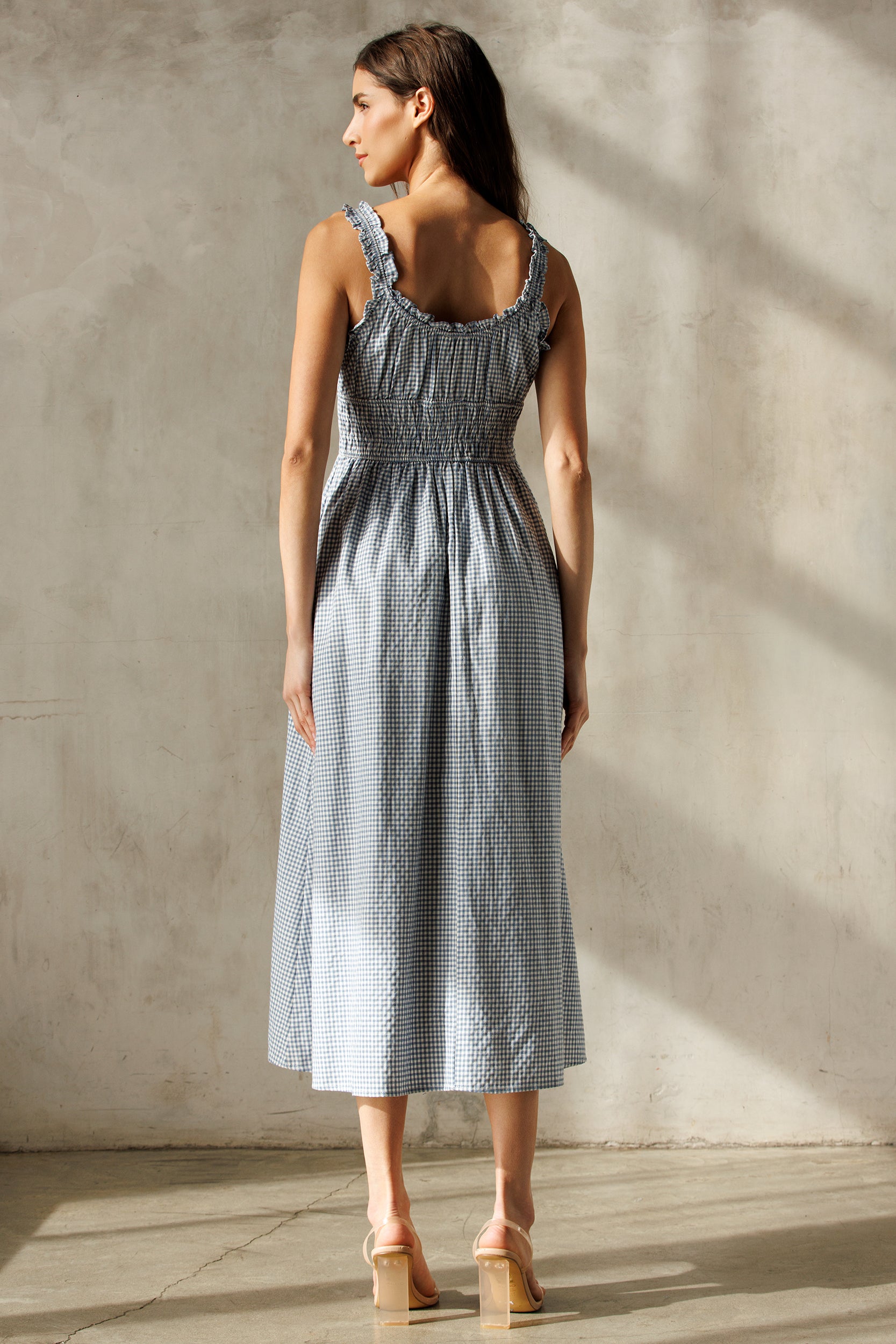Back view of a woman wearing a blue checkered dress against a neutral background