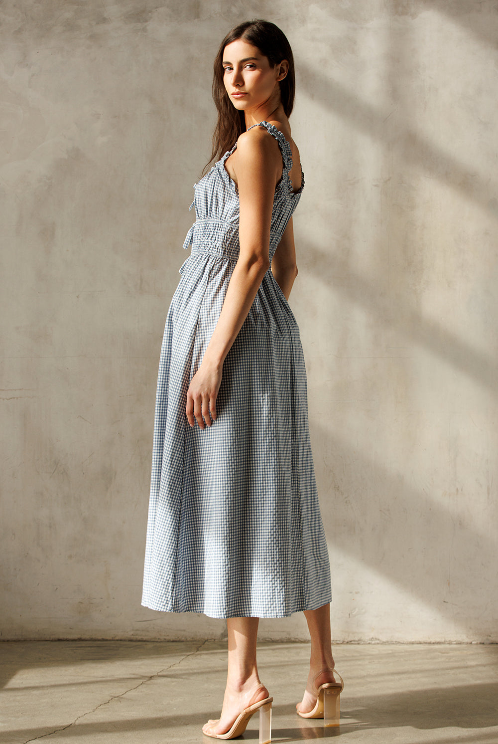 Side view of a woman wearing a blue checkered dress against a neutral background