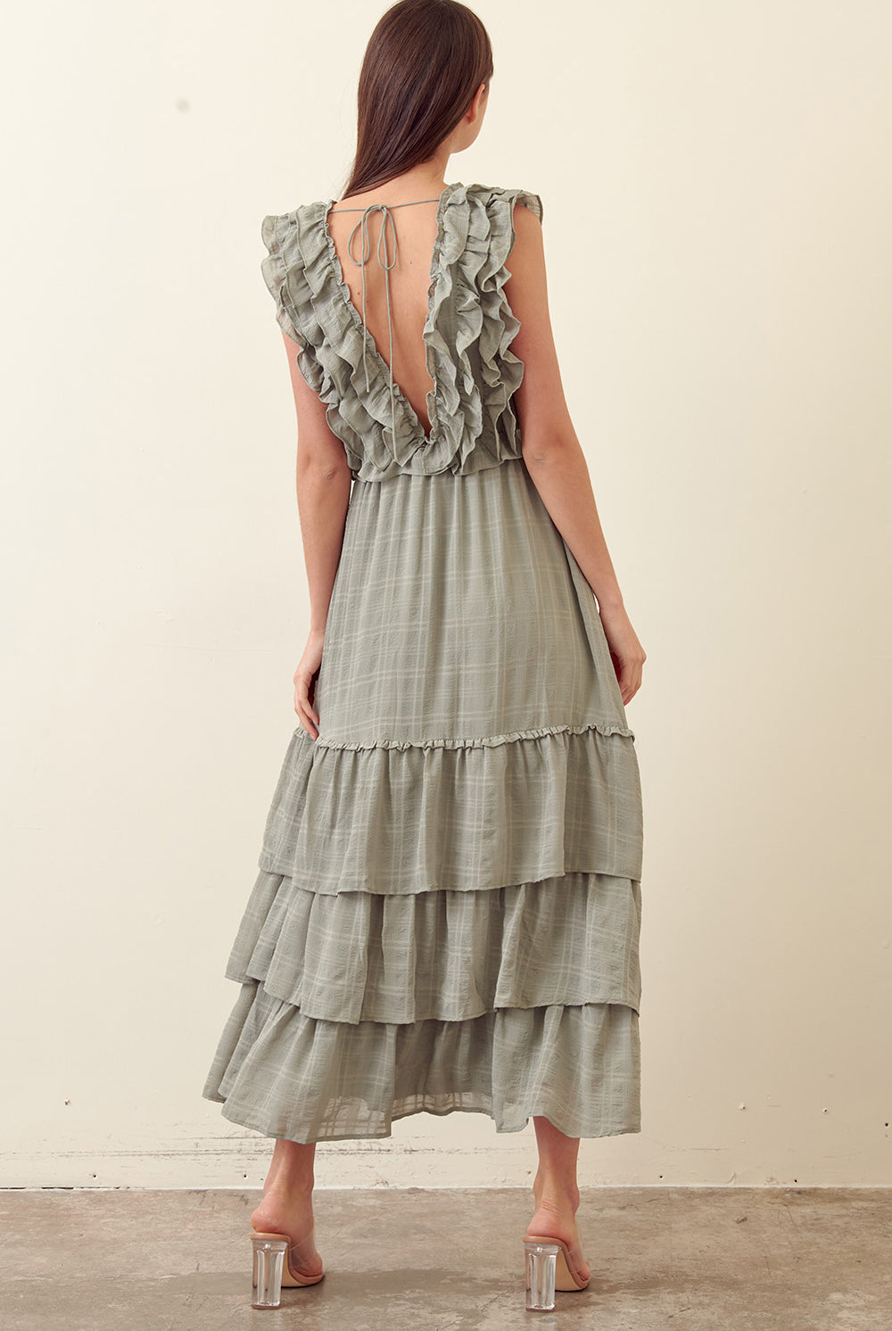 Back view of a woman wearing a green tiered dress against a plain background