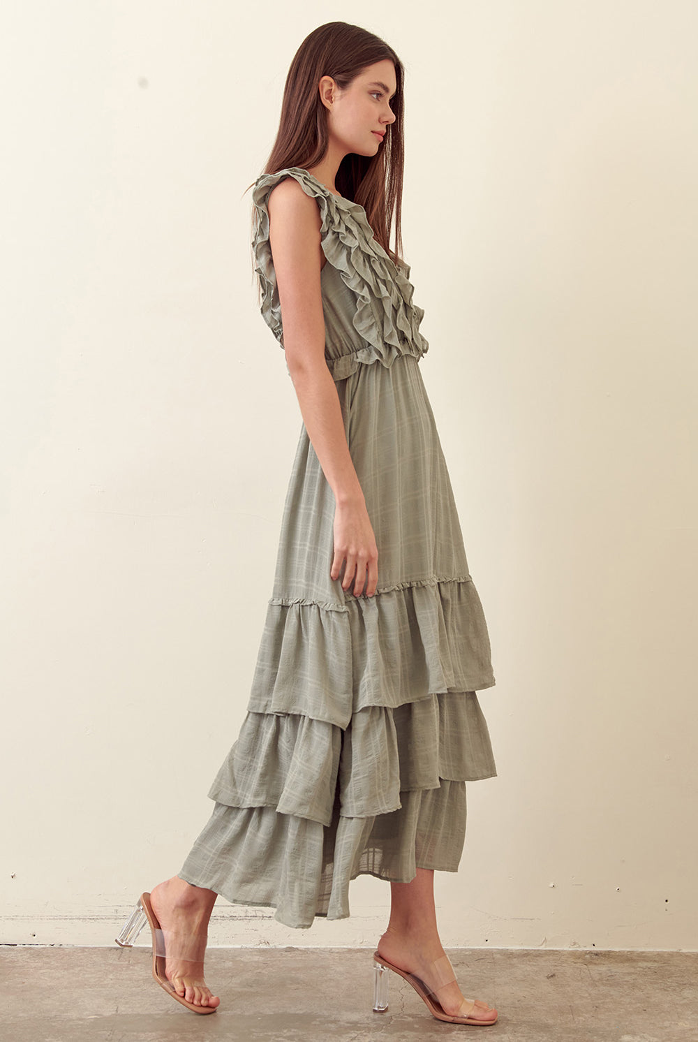 Side view of a woman wearing a green tiered dress against a plain background