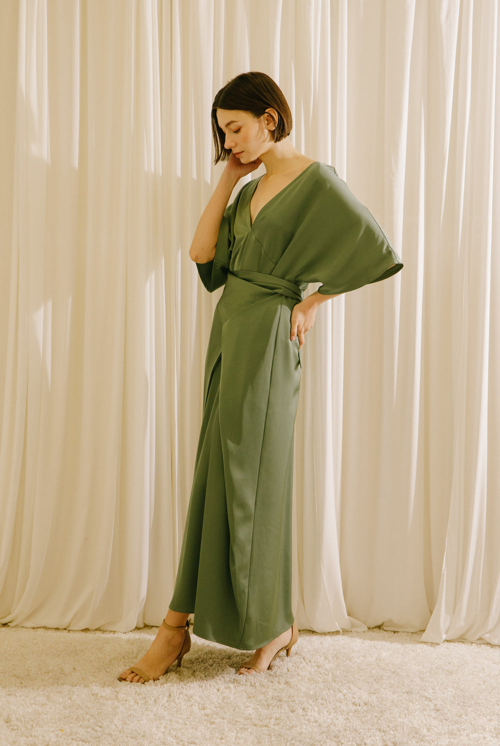 Side view of a woman wearing an olive green V-neck maxi dress with short sleeves and fluid drape