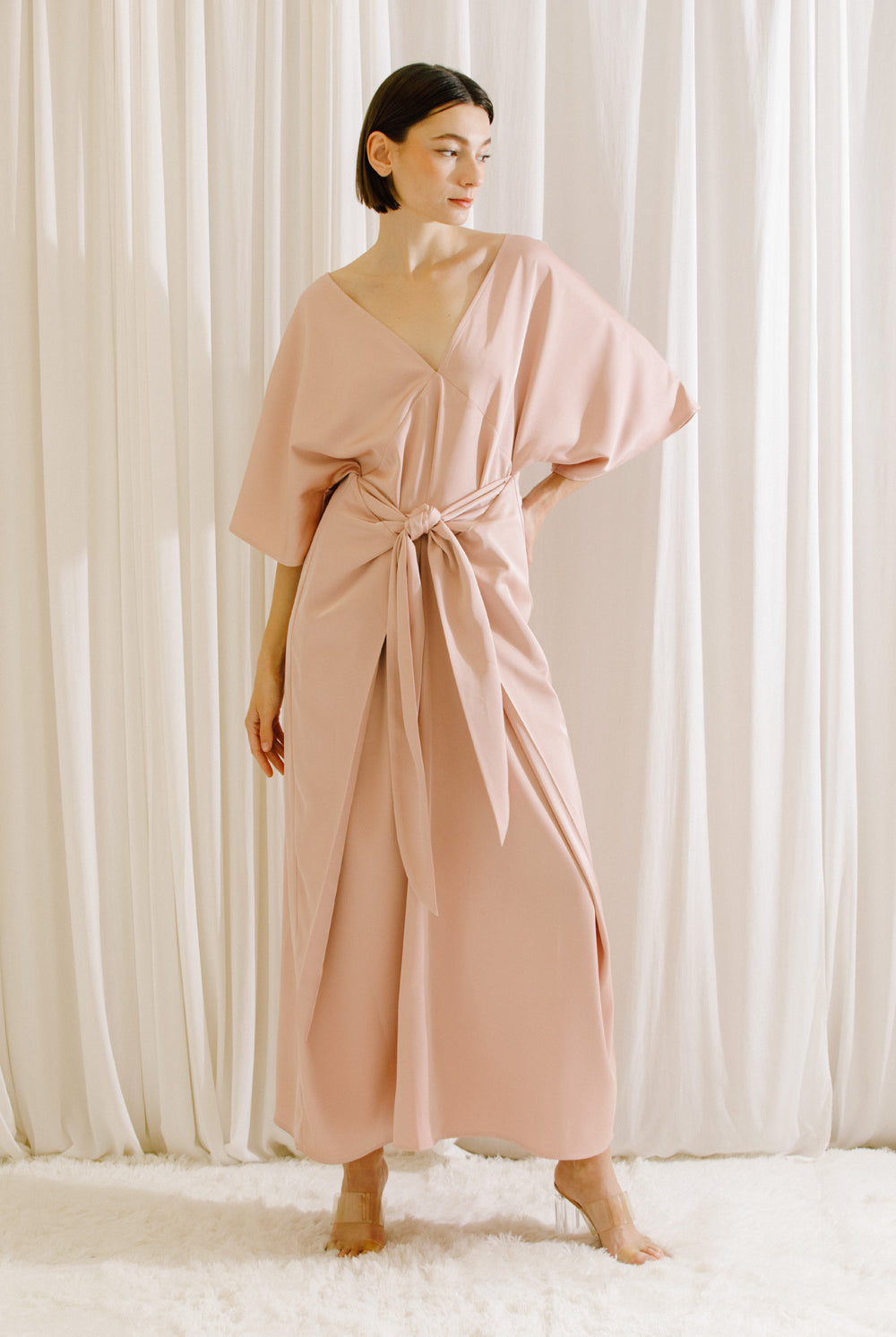 Front view of a woman wearing a pink V-neck maxi dress with short sleeves and fluid drape