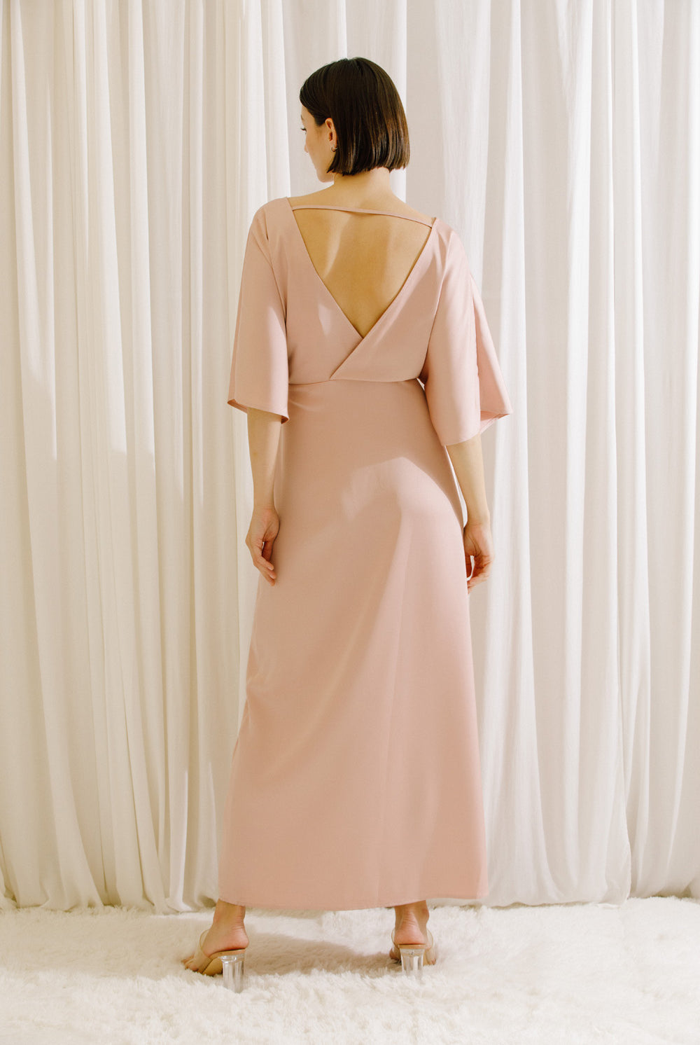 Back view of a woman wearing a pink maxi dress with short sleeves and fluid drape
