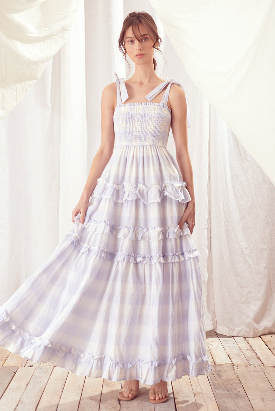Woman wearing a white dress and blue plaid against a white curtain background