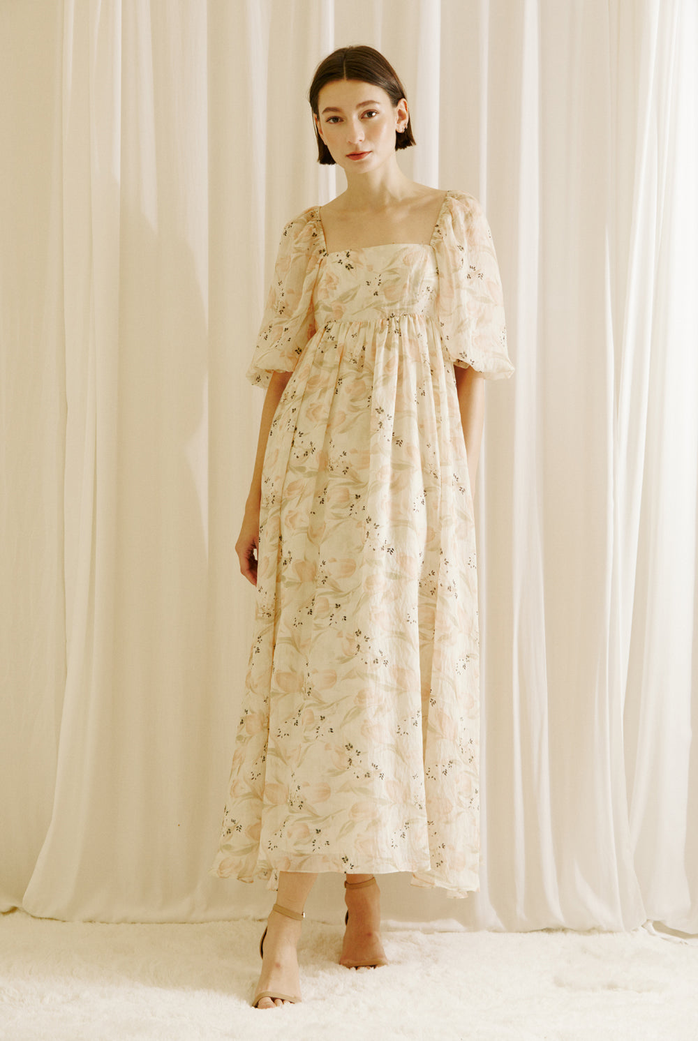 Woman wearing a floral dress with tulips print standing against a white curtain backdrop
