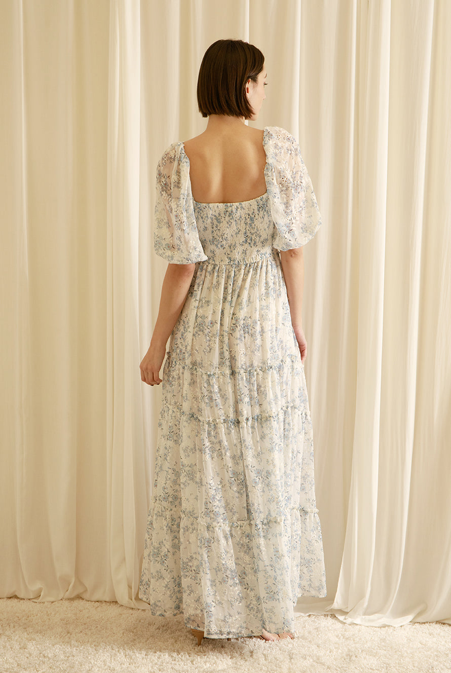 Back view of a woman wearing a floral dress standing in front of sheer curtains