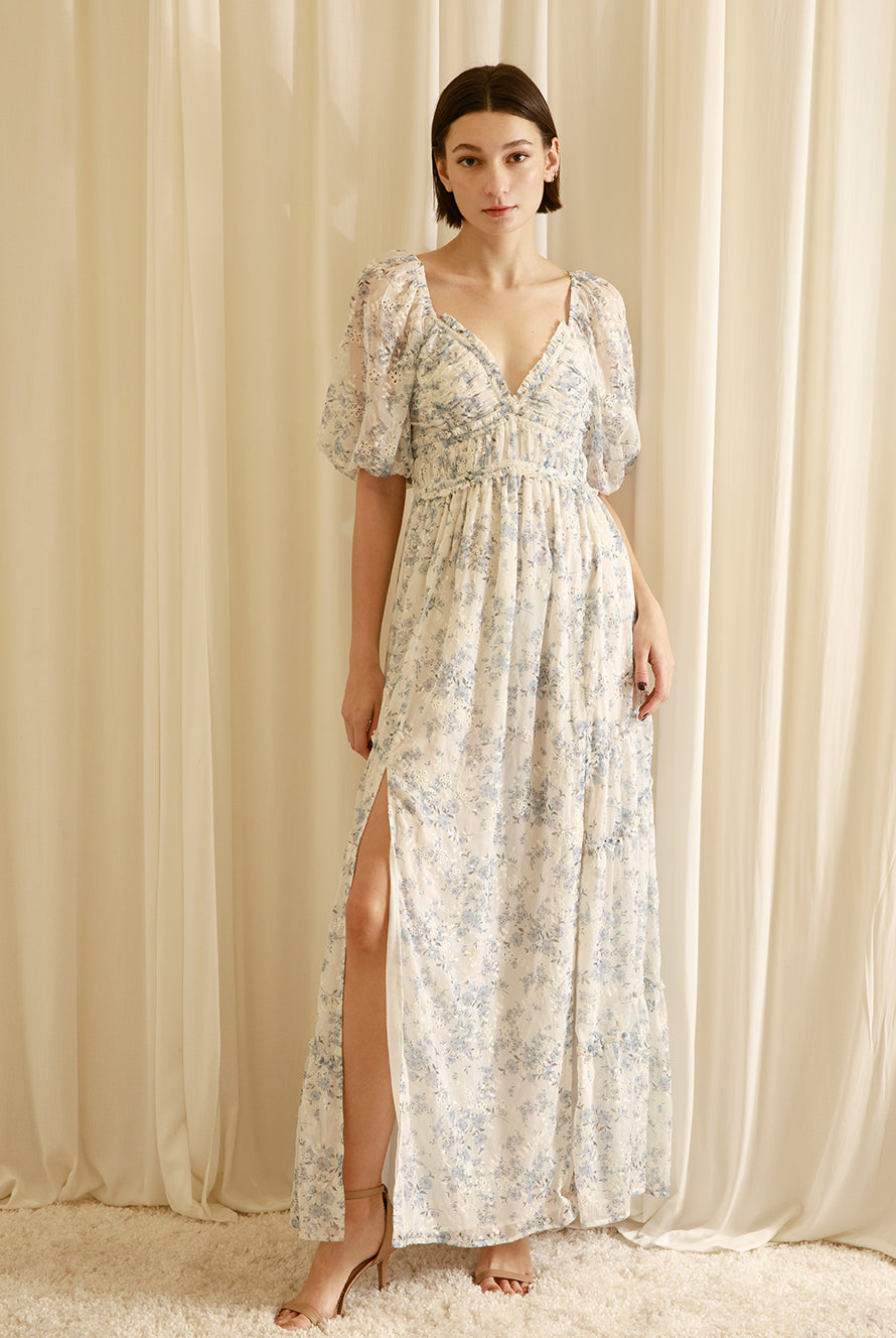 Woman wearing a floral dress with a slit in front against a beige curtain background