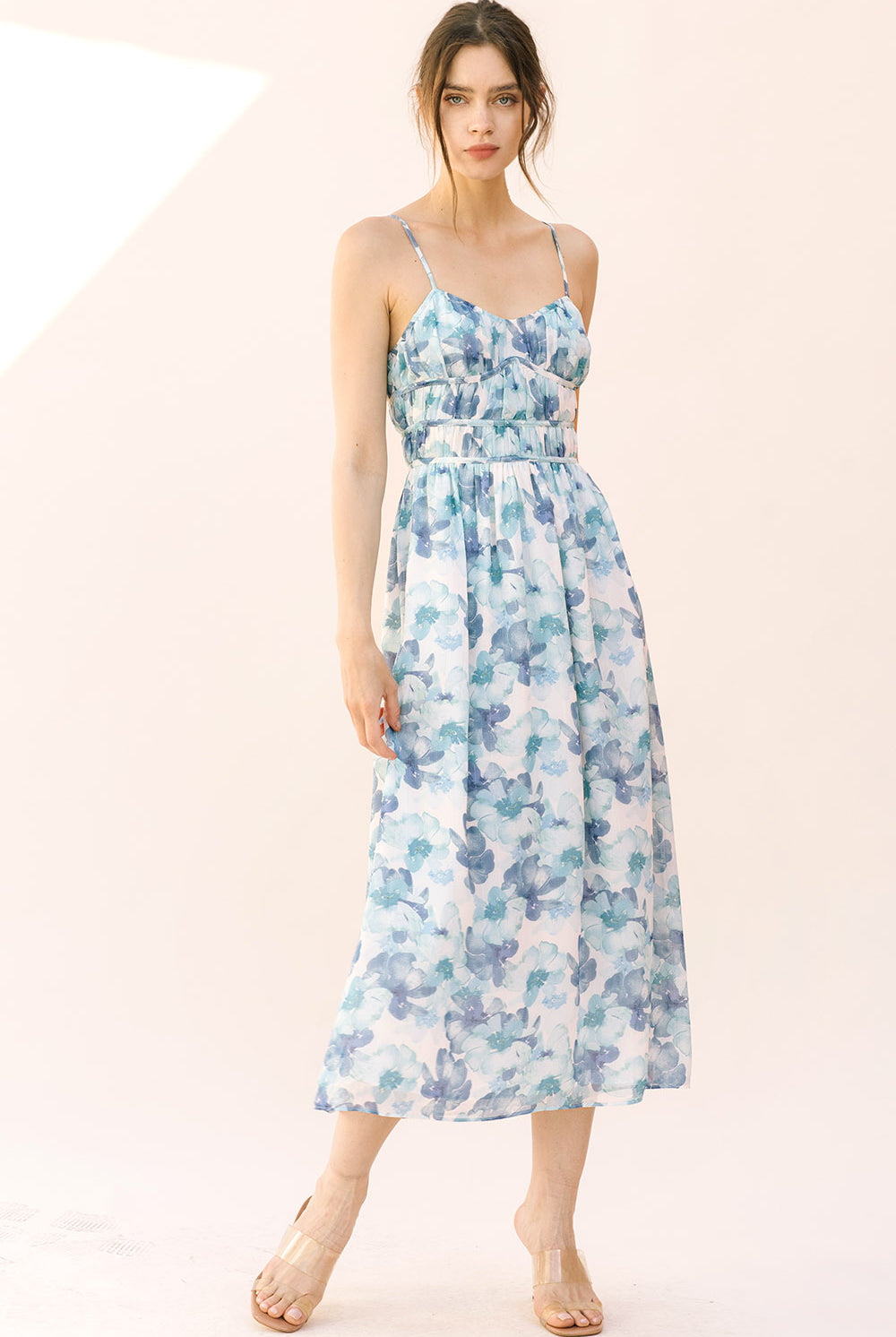 Woman wearing a blue floral midi dress with thin straps on a plain background