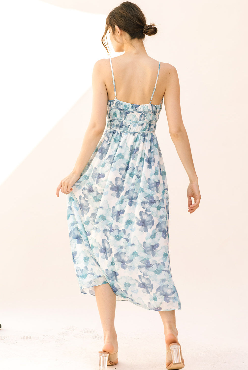Back view of a woman wearing a blue watercolor floral midi dress on a plain background