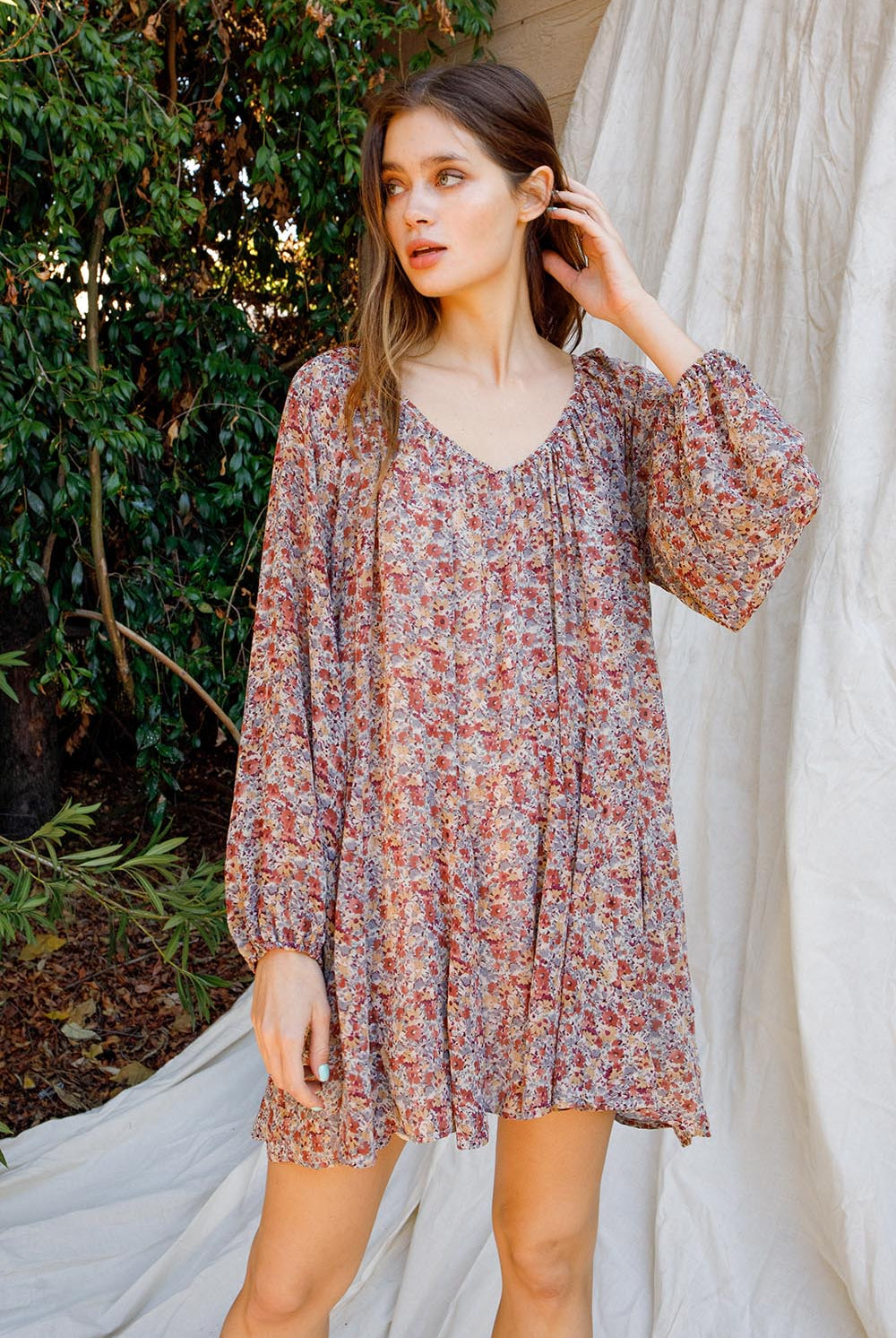 Woman wearing a floral dress standing outdoors with greenery in the background