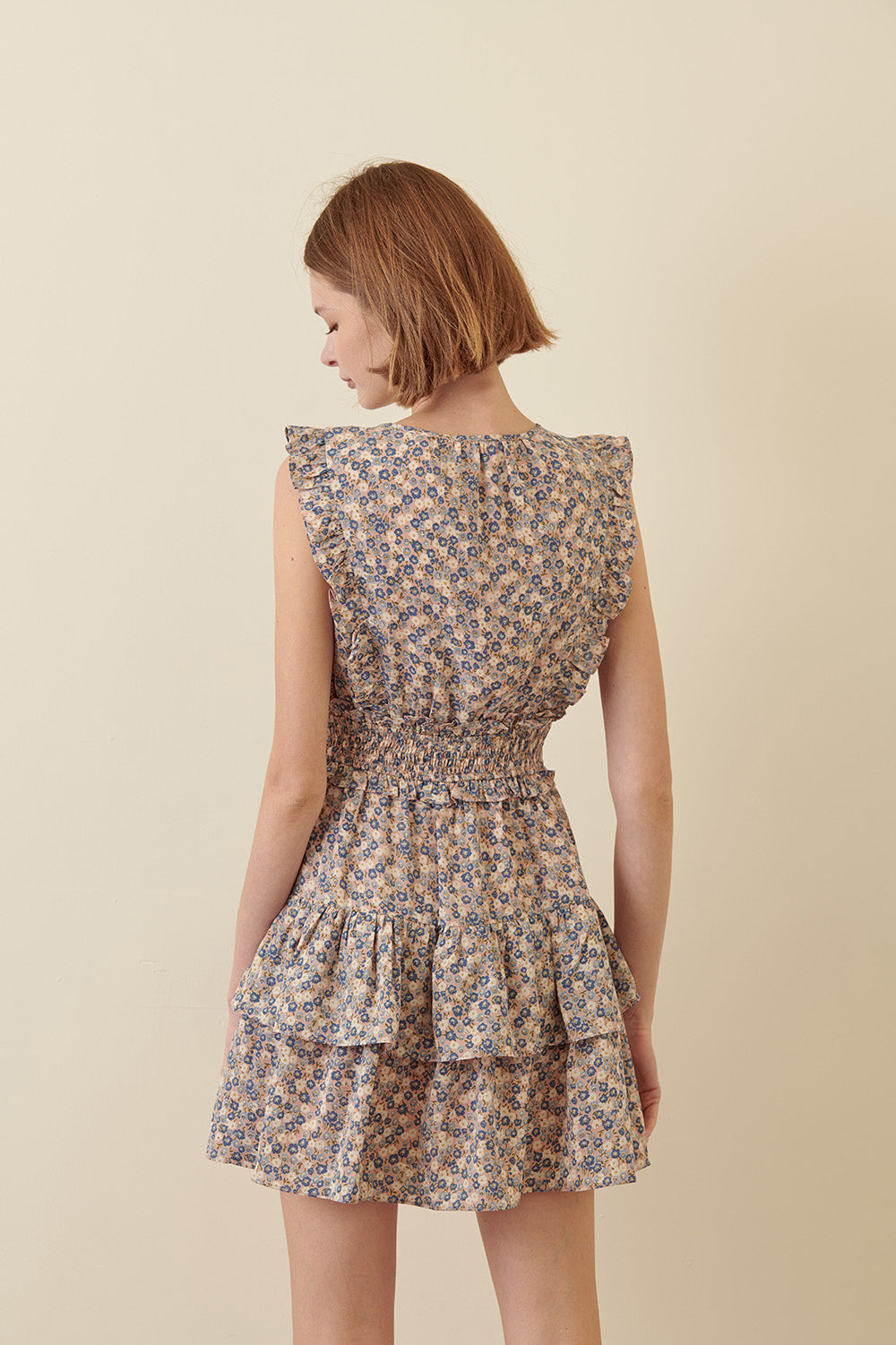 Back view of a woman wearing a blue floral dress on a beige background