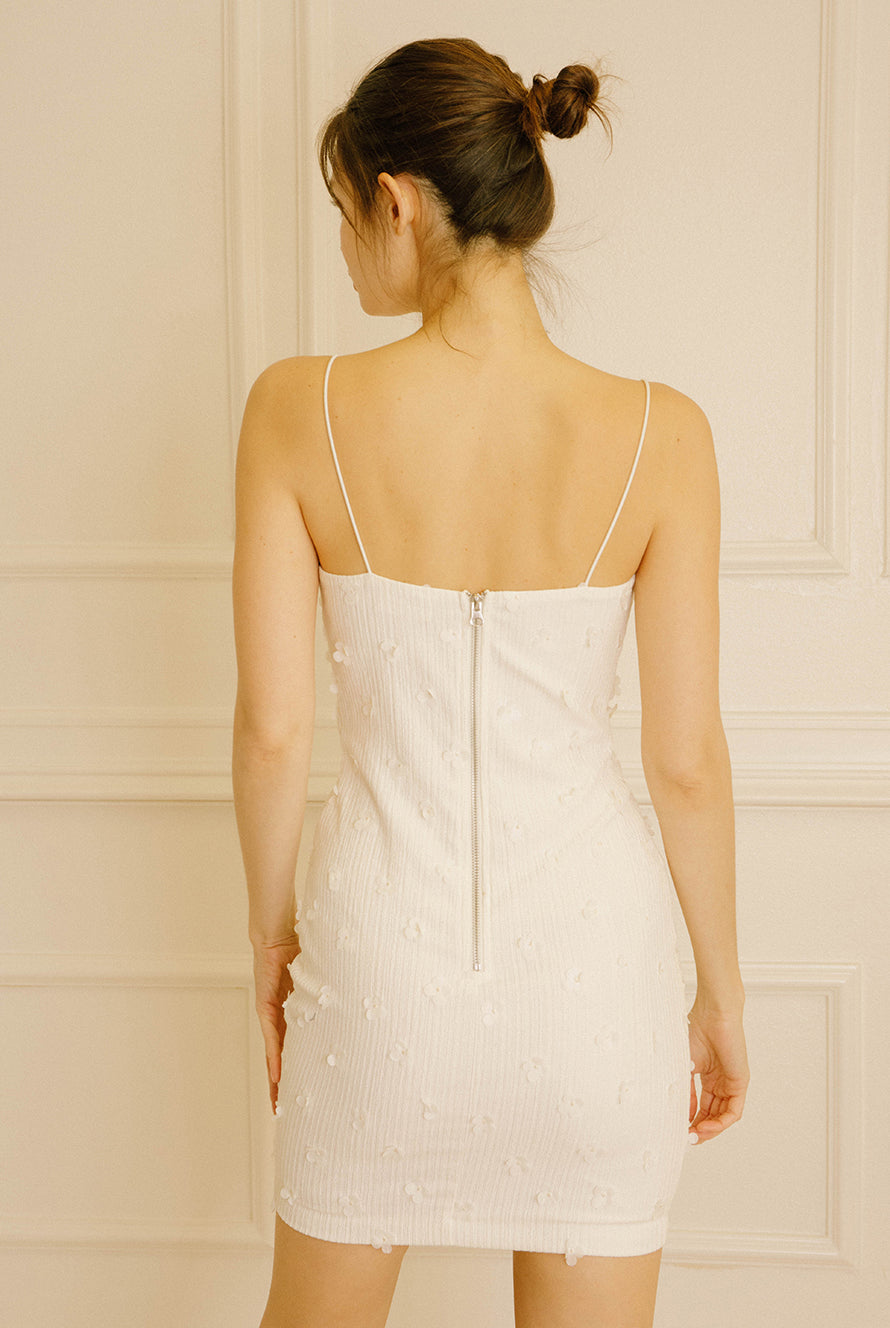 Back view of a woman wearing an ivory bodycon mini dress against a beige wall