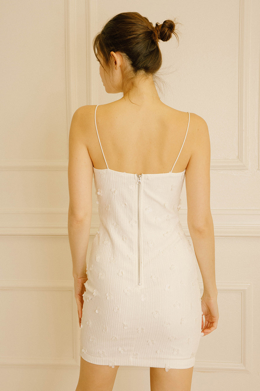 Back view of a woman wearing an ivory bodycon mini dress against a beige wall