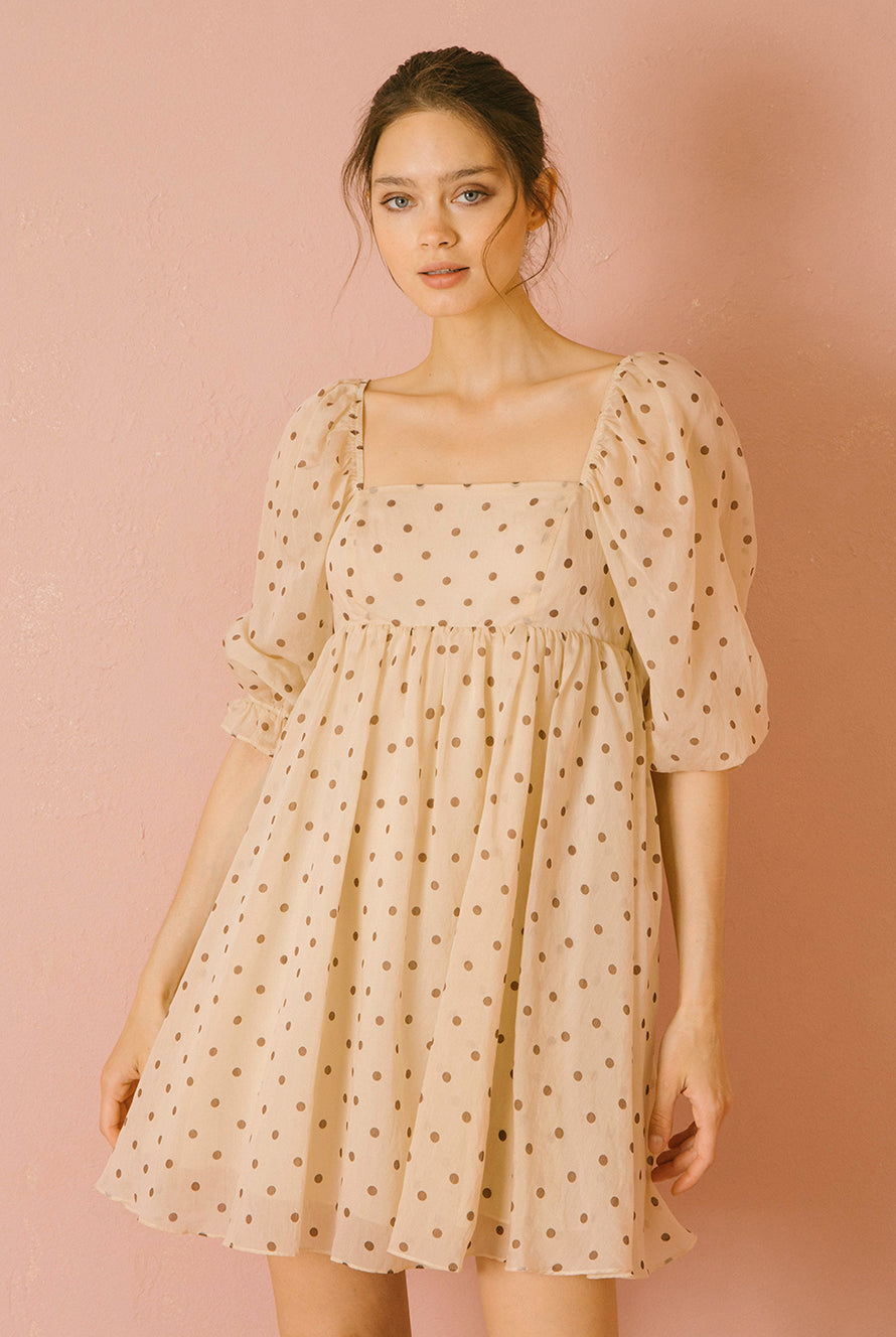 Woman wearing a beige polka dot dress against a pink background