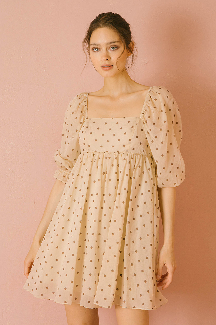 Woman wearing a beige polka dot dress against a pink background