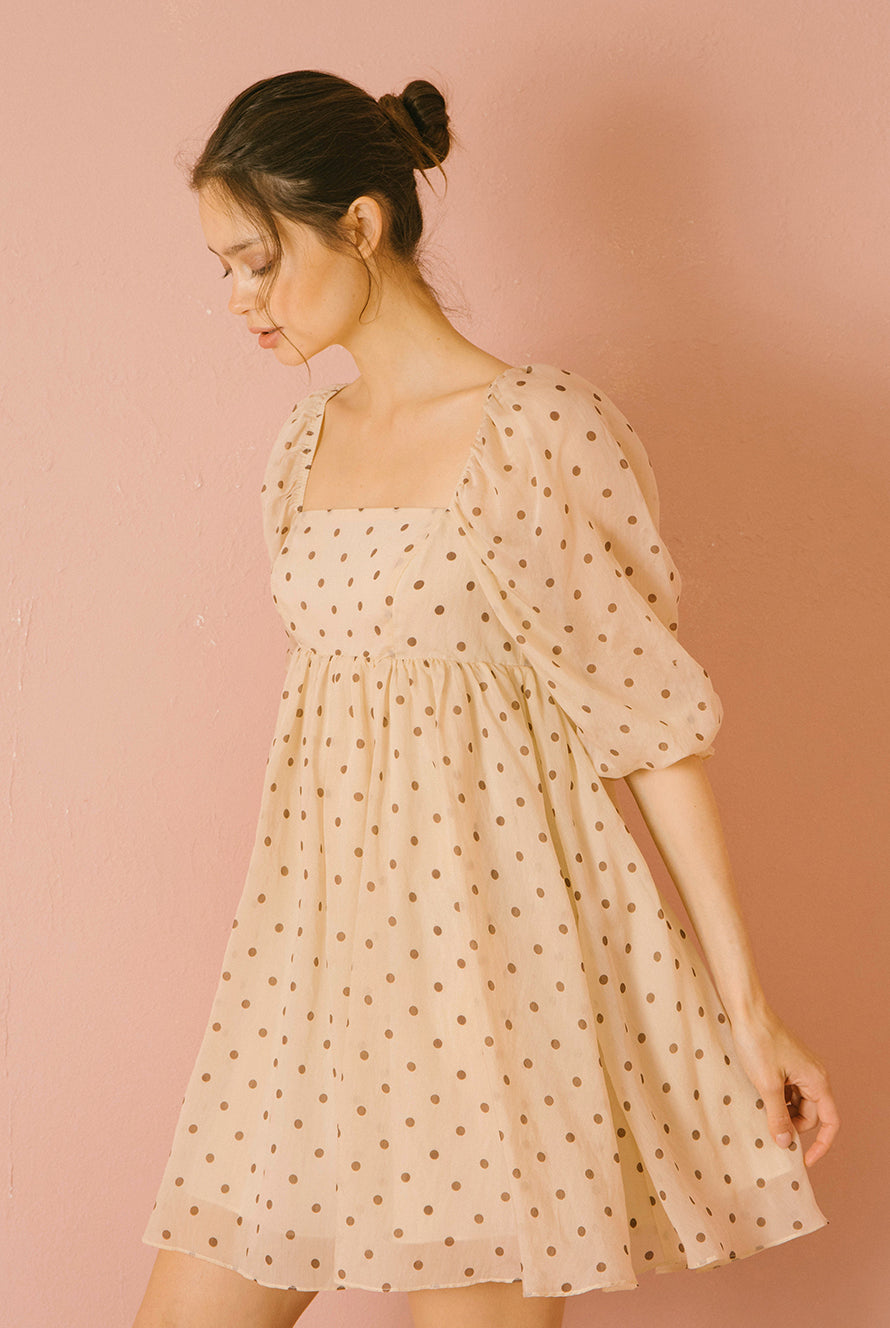 Side view of a model wearing a beige polka dot dress against a pink background
