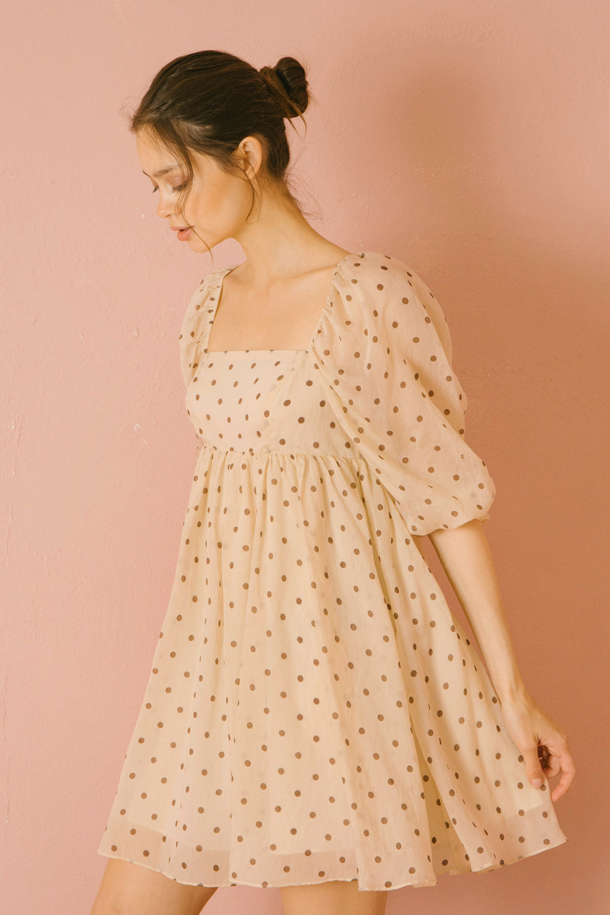 Side view of a model wearing a beige polka dot dress against a pink background