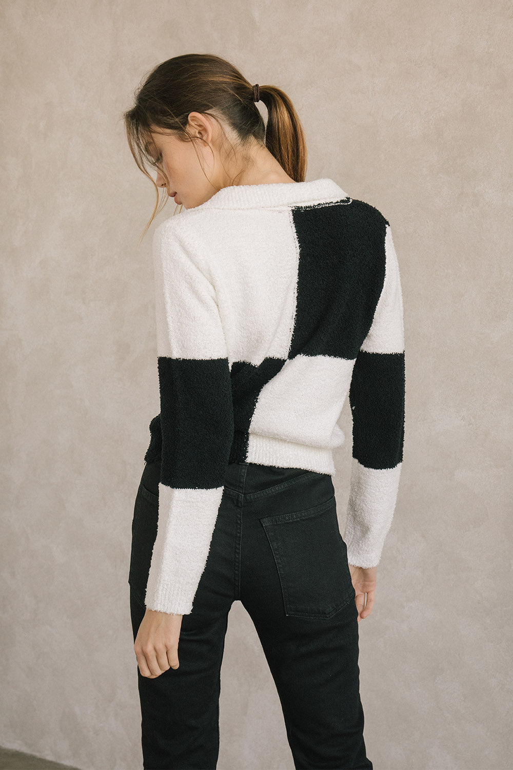 Back view of a woman wearing a black and white checkered zip-up sweater against a beige background