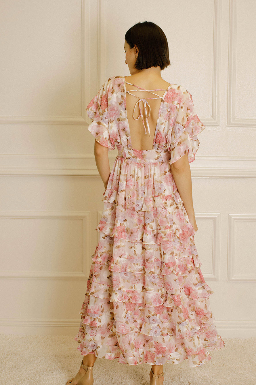 Woman wearing a pink and white floral dress with a backless design against a white paneled wall.