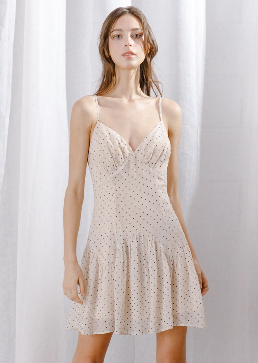 Woman wearing a beige dress with small hearts pattern against a white curtain background