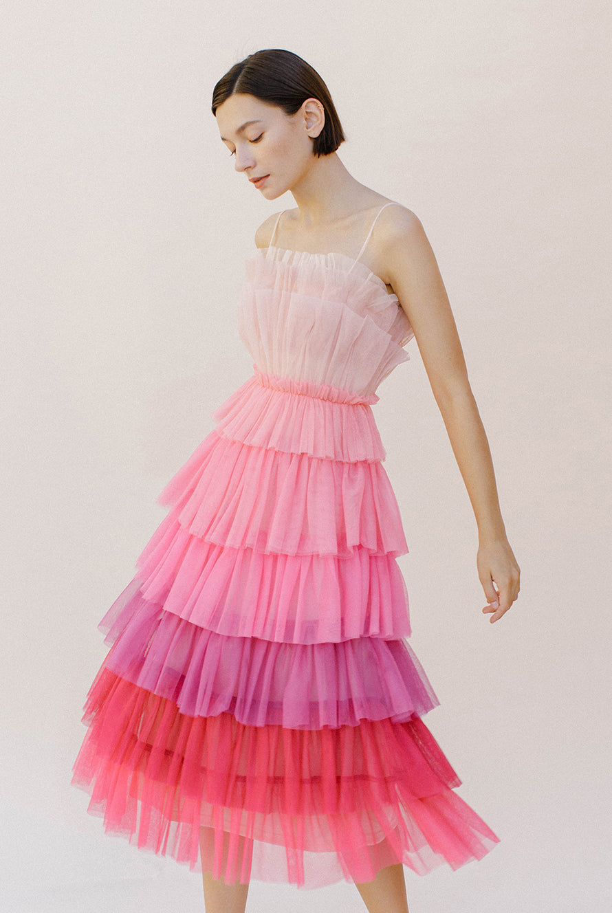 Woman wearing a pink ombre tulle tiered dress against a white background