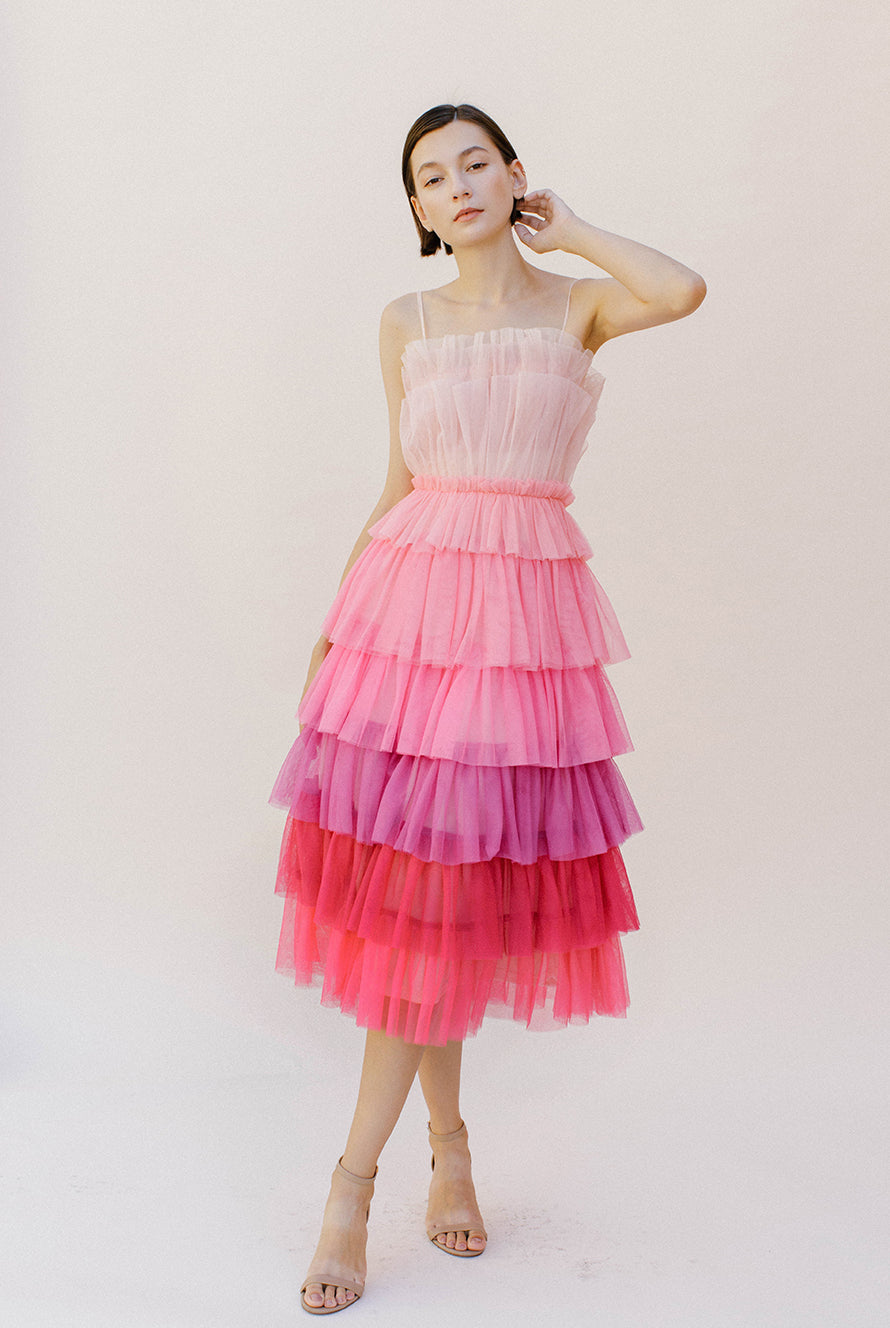 Woman wearing a pink tulle tiered dress against a white background