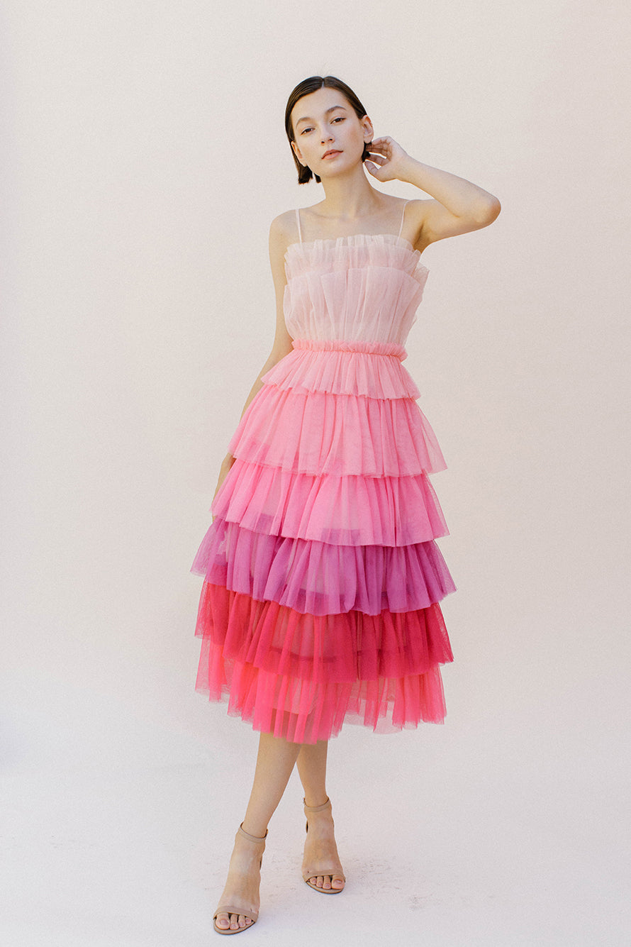 Woman wearing a pink tulle tiered dress against a white background