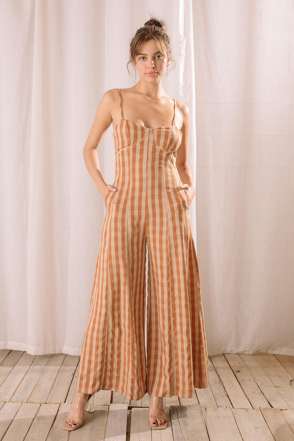 Woman wearing an orange checkered jumpsuit standing against a white curtain.