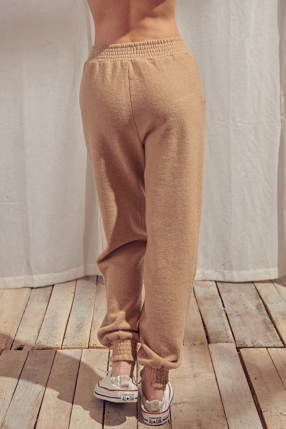 Back view of beige pants standing against a white curtain.